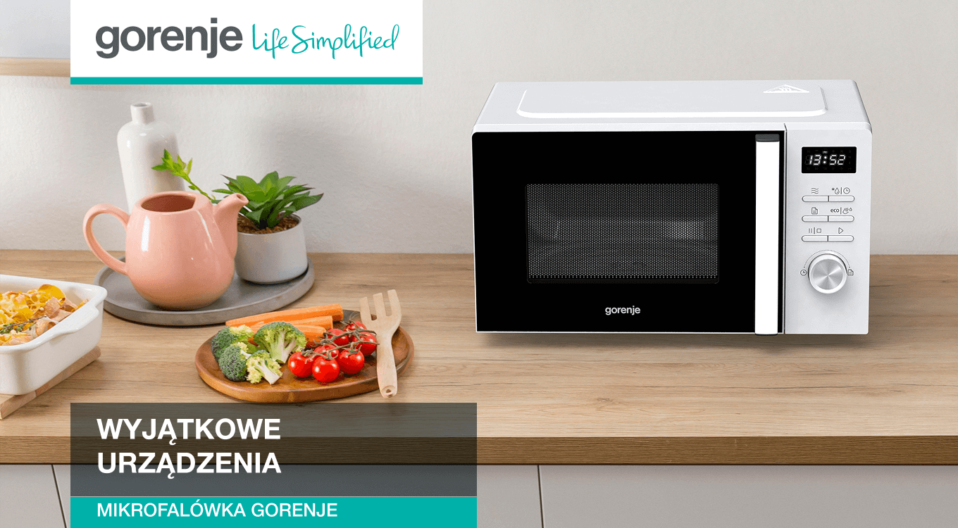 Biała kuchenka mikrofalowa marki Gorenje stojąca na drewnianym blacie kuchennym. Obok znajdują się warzywa na desce do krojenia oraz ceramiczny dzbanek. W lewym górnym rogu widoczne logo Gorenje z hasłem „Life Simplified”.