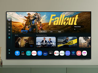 Ekran telewizora smart TV Samsung QLED Q7F2 2025 z systemem operacyjnym Tizen, widziany od przodu, powieszony na szarej ścianie, a na nim wyświetlane treści i aplikacje.