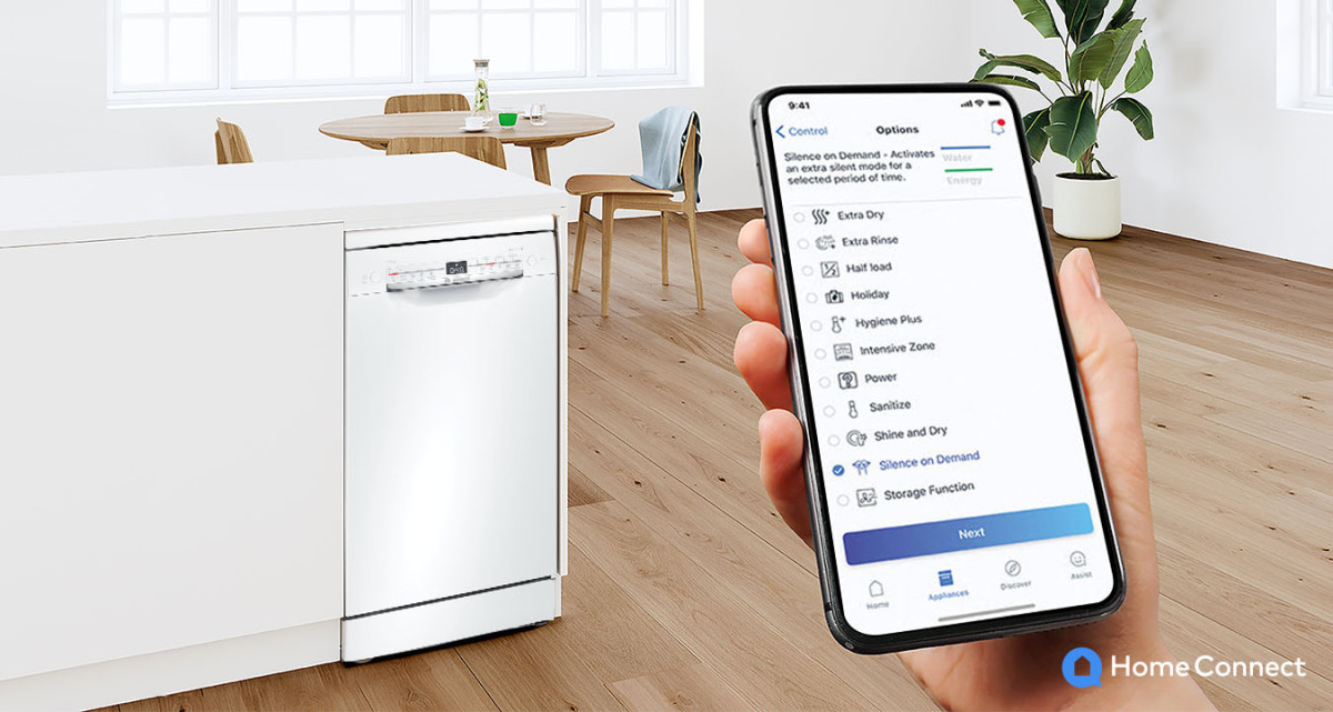 Ręka trzymająca smartfon, na nim aplikacja Home Connect z wyborem trybu pracy zmywarki. w tle Zmywarka marki Bosch