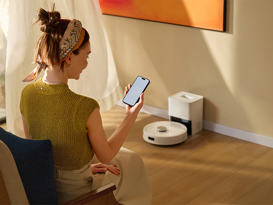Kobieta w jasnym salonie steruje robotem Roborock Q7 TF White za pomocą aplikacji mobilnej