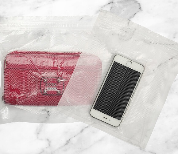Czerwony portfel i biały smartfon zapakowane w przezroczyste plastikowe torby leżące na marmurowym blacie.