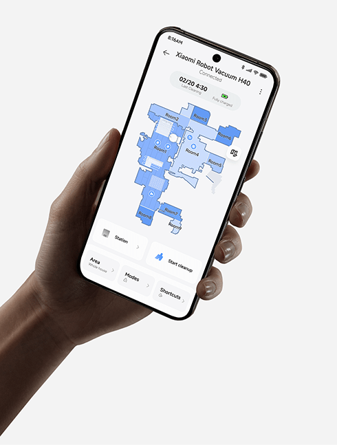 Dłoń trzymająca smartfon z aplikacją sterującą robotem sprzątającym Xiaomi Robot Vacuum H40, pokazującą mapę mieszkania z podziałem na pokoje i opcjami czyszczenia.
