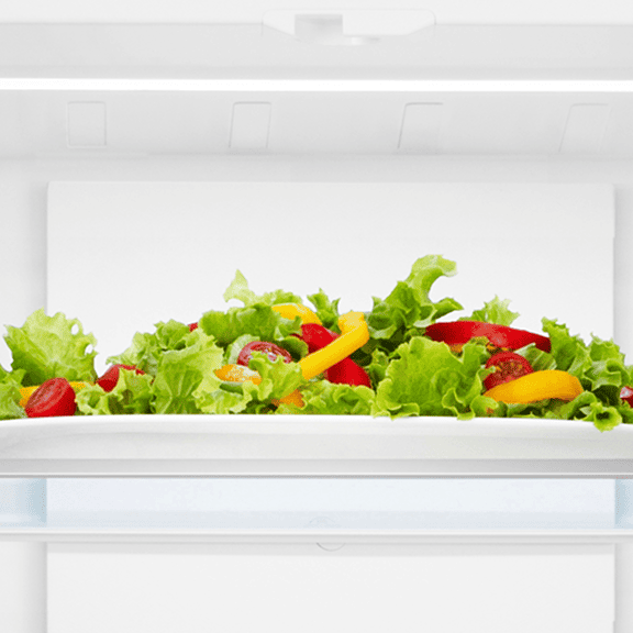 Oświetlenie LED wewnątrz lodówki Gorenje, równomiernie podświetlające półkę z talerzem świeżej sałatki. (120 znaków)
