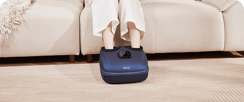 Zbliżenie na nogi kobiety korzystającej z masażera stóp SKG YS100 siedząc w salonie na kanapie