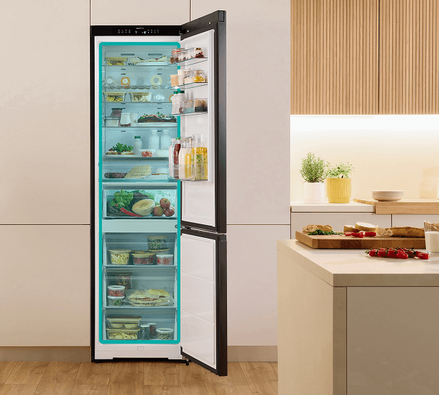 Otwarta lodówka w jasnej obudowie Gorenje wypełniona produktami i z zaznaczoną na niebiesko częścią chłodziarki i zamrażarki