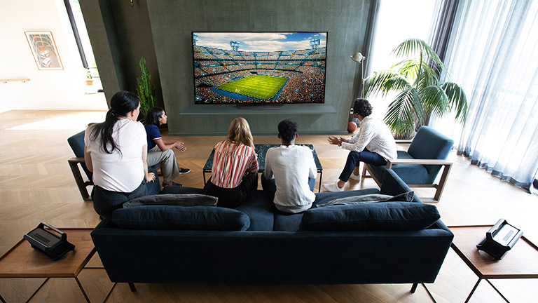 Ludzie oglądający sport w telewizji w salonie z podłączonymi tylnymi głośnikami Bluetooth