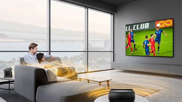 Mężczyzna i kobiety oglądają sport w telewizji w salonie z podłączonymi tylnymi głośnikami Bluetooth