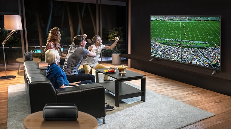 Ludzie oglądający sport w telewizji w salonie z podłączonymi tylnymi głośnikami Bluetooth.