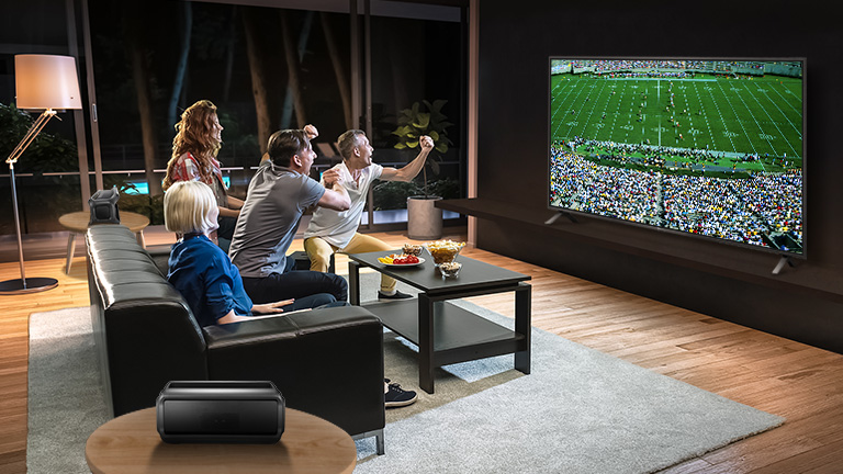 Ludzie oglądający sport w telewizji w salonie z podłączonymi tylnymi głośnikami Bluetooth.