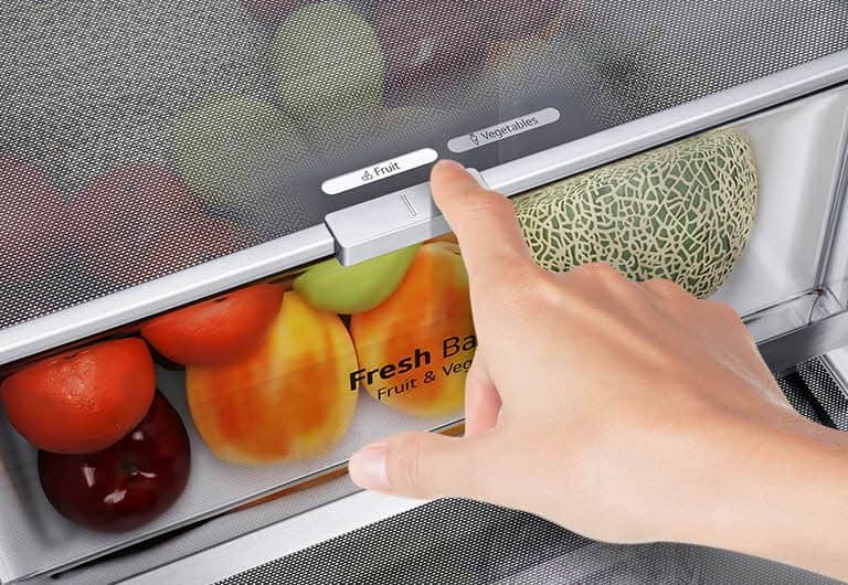 Dolne szuflady lodówki są wypełnione kolorowymi produktami spożywczymi. Zdjęcie we wstawce pokazuje w powiększeniu dźwignię wyboru optymalnego poziomu wilgotności pozwalającego utrzymać świeżość produktów.