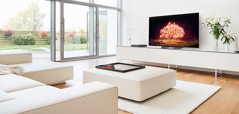 Telewizor przedstawiający drzewo emitujące czerwone światło w białym i prosto urządzonym wnętrzu domu.