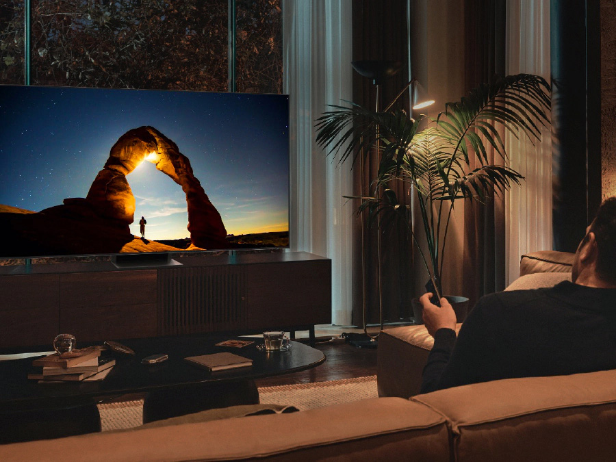 Mężczyzna przed telewizorem QLED w nocy. Ekran wyświetla obraz zoptymalizowany w Trybie Komfortu dla Oczu.