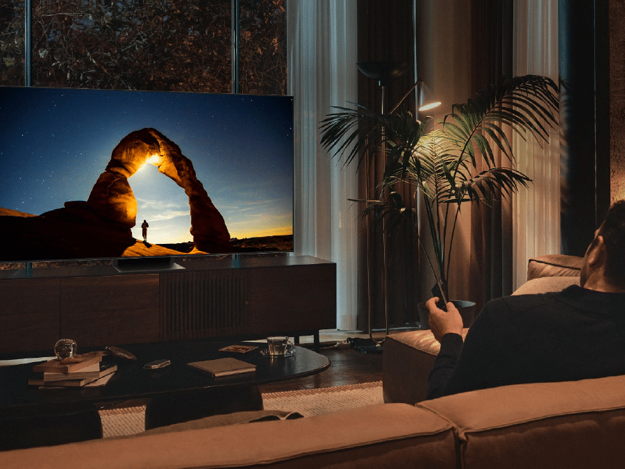 Mężczyzna przed telewizorem QLED w nocy. Ekran wyświetla obraz zoptymalizowany w Trybie Komfortu dla Oczu.