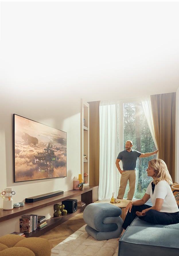 Duży telewizor znajduje się w jasnym salonie z roślinami i różnymi ozdobami.