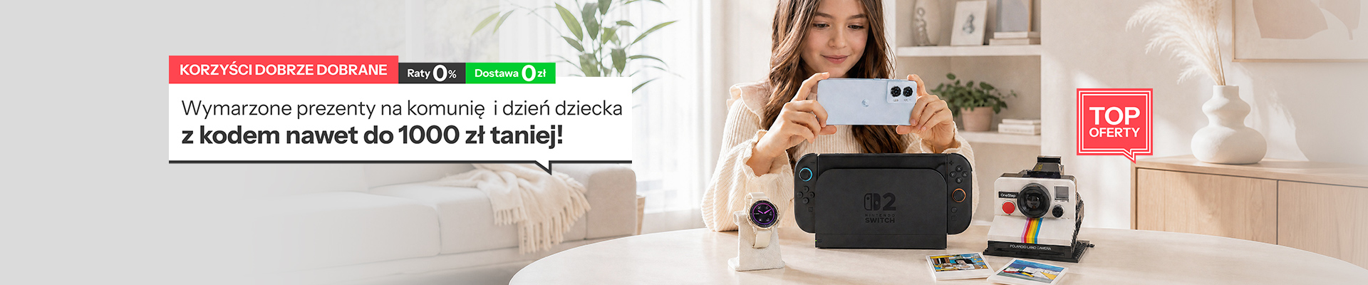 Dziewczynka robiąca zdjęcie smartfonem. Przed nia na stole konsola nintendo switch, aparat i smartwatch.